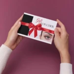 Holding a beauty gift voucher with red ribbon.